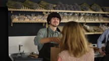 Smiling young cashier giving paper bag to the female customer. Woman leaves with smile on her face. Happy Father and son high five in family bakery.