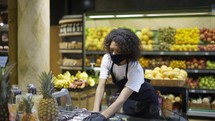 Female grocery store employee in face mask and gloves checking freshness of products in store.