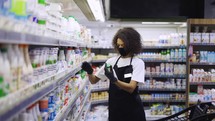 Female worker arranging products on shelves in milk department in food store.