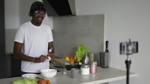 African man standing in kitchen records on cellphone new food videoblog in the morning.