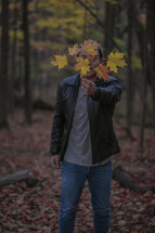 a man holding a branch full of fall leaves in front of his face 