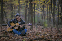 a man sitting in a forest playing a guitar 