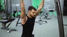 Male training back and hands muscles doing pulls weight exercise in a gym