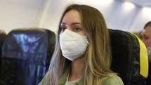 Blonde woman in white respirator inside the airplane.