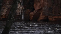 Waves and ripples forming in a forest river with a strong current, slow motion view with brown cliffs in the background