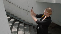 A young woman, wearing a black suit and white-framed sunglasses, is taking a selfie on her mobile phone on the steps at the entrance of the subway