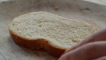 A close-up of a person's hand spreading orange marmalade on a piece of white bread