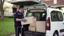 Young handsome Caucasian delivery man putting boxes in van delivering shipment. Male post office worker Courier concept.