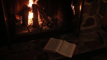open Bible near a fire in a hearth 