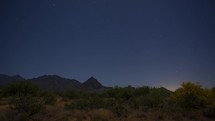 Timelapse of stars beyond a mountain range and colorful desert plants 