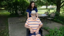 A caregiver with an elderly man in a wheelchair outdoors