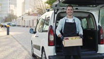 Happy smiling man with braces holding wooden box with apples at street outdoors, portrait of happy deliveryman in apron and gloves. Online shopping delivering, smart vegetables express delivery service, slow-motion.