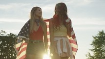 young women walking with an American flag draped over their backs 