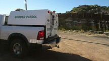 Border Patrol trucks park by the fence at the border with Mexico