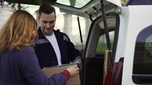 A woman receives a cardboard box from a handsome delivery man outdoor.