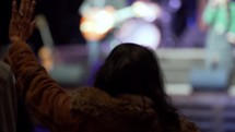 A woman waves her hand in praise to worship music