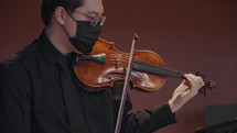 A masked violinist plays the violin. 
