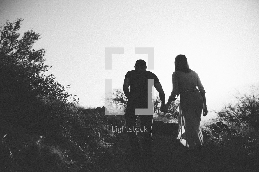 Silhouette of a couple walking up a hill.