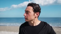 Man Looks Around Dressed In Black And On The Beach Near The Sea