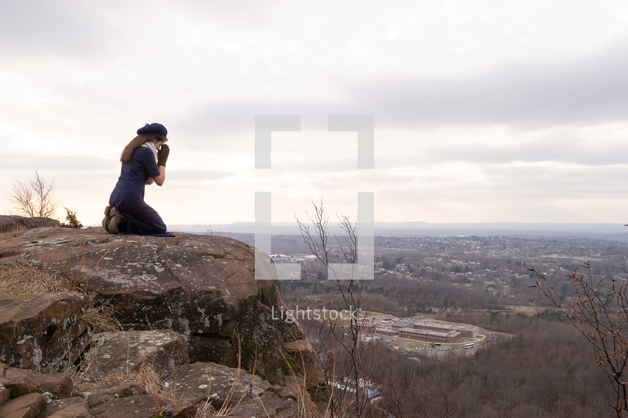 a woman kneeling in prayer on a mountaintop 