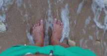 Top view of a man feet standing on a sandy beach shore.

