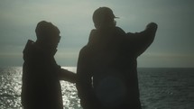 men pointing out at the ocean 