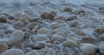 Sea foam washing over large stones on the shore.