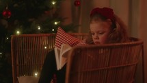 A little girl reading the bible by the Christmas tree