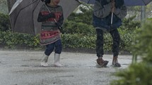 Boy and a girl jumping with umbrellas in the pouring rain in slow motion