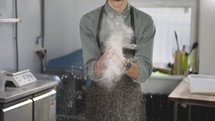 Handsome male baker claps and scatters white flour in the air. Young man making homemade bread claps with a handful of organic whole wheat flour in each hand. Slow motion, close up.