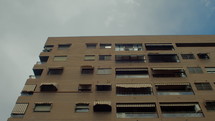 Low angle shot - a residential multi-storey building with closed blinds on the windows and glazed balconies