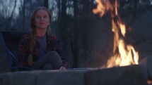 Young woman enjoying the warmth of a campfire at dusk