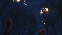 Smiling woman celebrating with sparklers at dusk