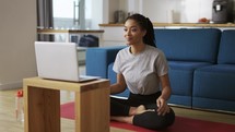Young African woman doing yoga sitting in front the laptop.