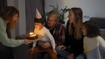 Little boy blows out the candles on dream the cake in a circle of happy family.