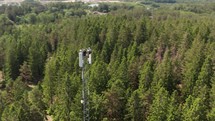 Skyward Ascent: Drone View of Telecom Technicians Scaling Forest Tower Heights