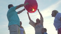 Steadicam shot of mother, son and grandparents flying paper lantern on summer day with following view to the lantern getting higher in clear blue sky