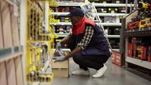 Male worker refill goods on lower shelves of hardware store.