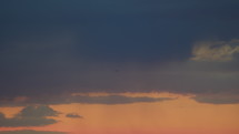 The plane is making a turn against the backdrop of a yellow-red sunset sky and dark clouds. Its navigation lights are flashing as it smoothly gains altitude