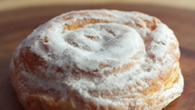 A close-up of a sweet, wheat bun covered with powdered sugar and sprinkled with cinnamon dust