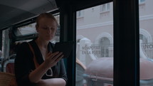 Slow motion - a young woman holds an e-book in her hand and reads something while traveling around the city by bus, standing at the door