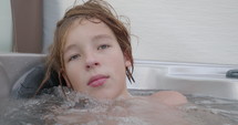 A teenager enjoys in a hot tub, surrounded by water bubbles, dreamily contemplating and savoring the momen