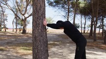 Man with Black Tracksuit Stretches in a Pine Tree