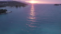 Slow aerial tilt up of turquoise waters to picturesque sunset on Ionian Sea coast.