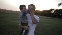 Happy father and son. A loving father playing with his happy young boy, holding and hugging him affectionately in the evening sunset or sunrise sunlight in cinematic slow motion.