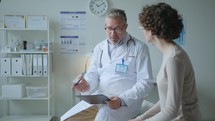 Doctor Talking to Patient Sitting on Examination Table in Medical Office
