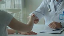 Doctor Greeting Patient with Handshake and Giving Consultation in Clinic
