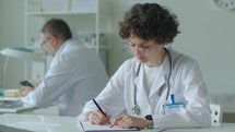 Female Doctor Filling Out Paper Form at Work in Medical Office
