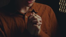 Close-up shot of young female penitent sitting in confessional booth and praying with hands clasped
