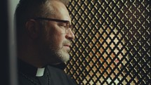 Senior priest in cassock talking to penitent sitting behind latticed screen during confession in church. Close-up view
